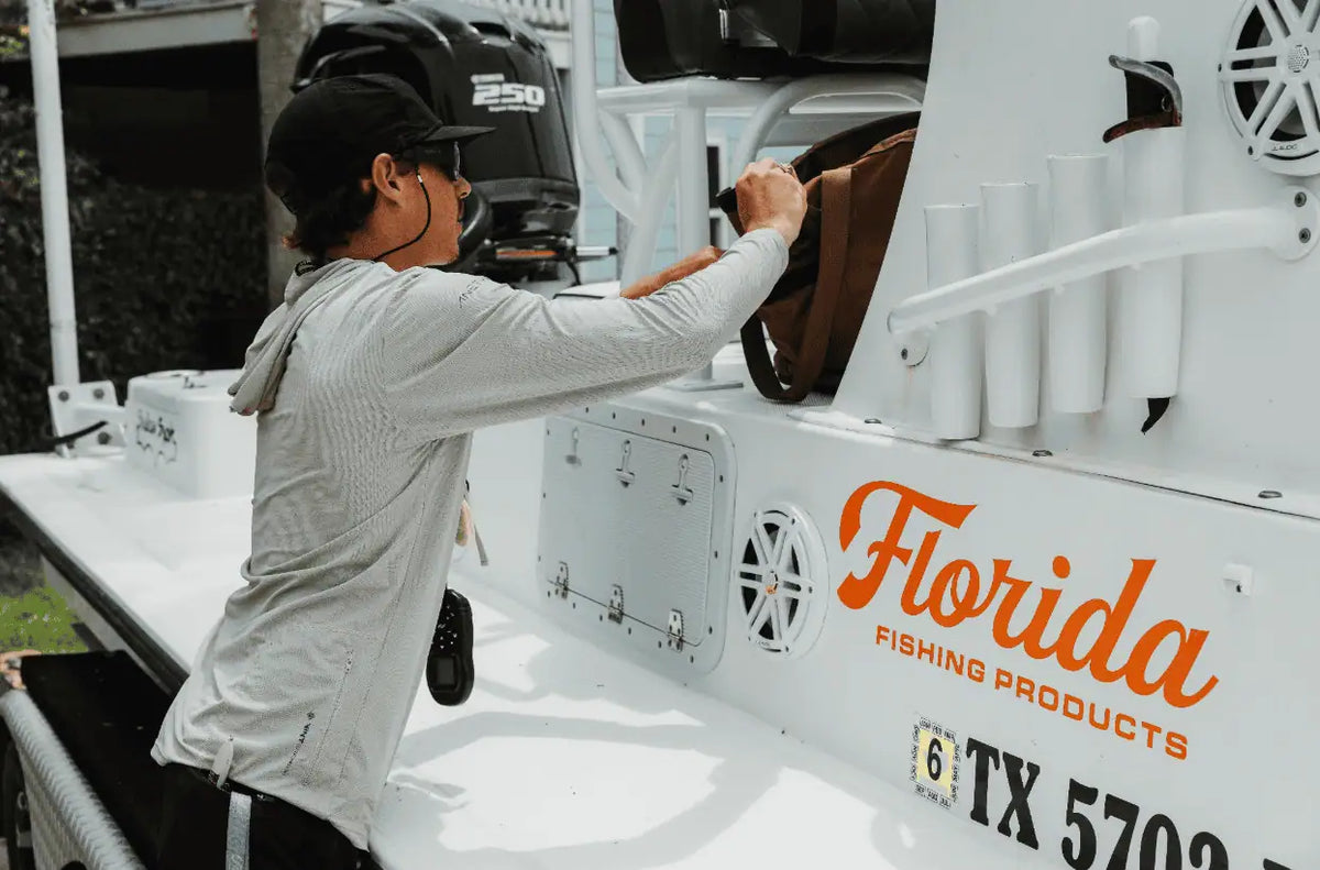 Man loading fishing gear onto a white boat branded with the Florida Fishing Products logo.