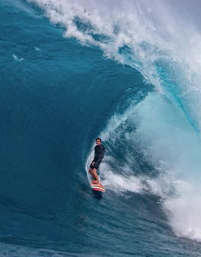 Albee Layer of Anetik wearing performance activewear surfing a large ocean wave