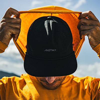 Person wearing an ANETIK hooded sun shirt pulling the hood up over a black ANETIK cap outdoors.
