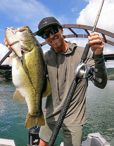 Jason Selgert of Anetik wearing performance fishing hoodie holding a large bass on a boat in a freshwater lake