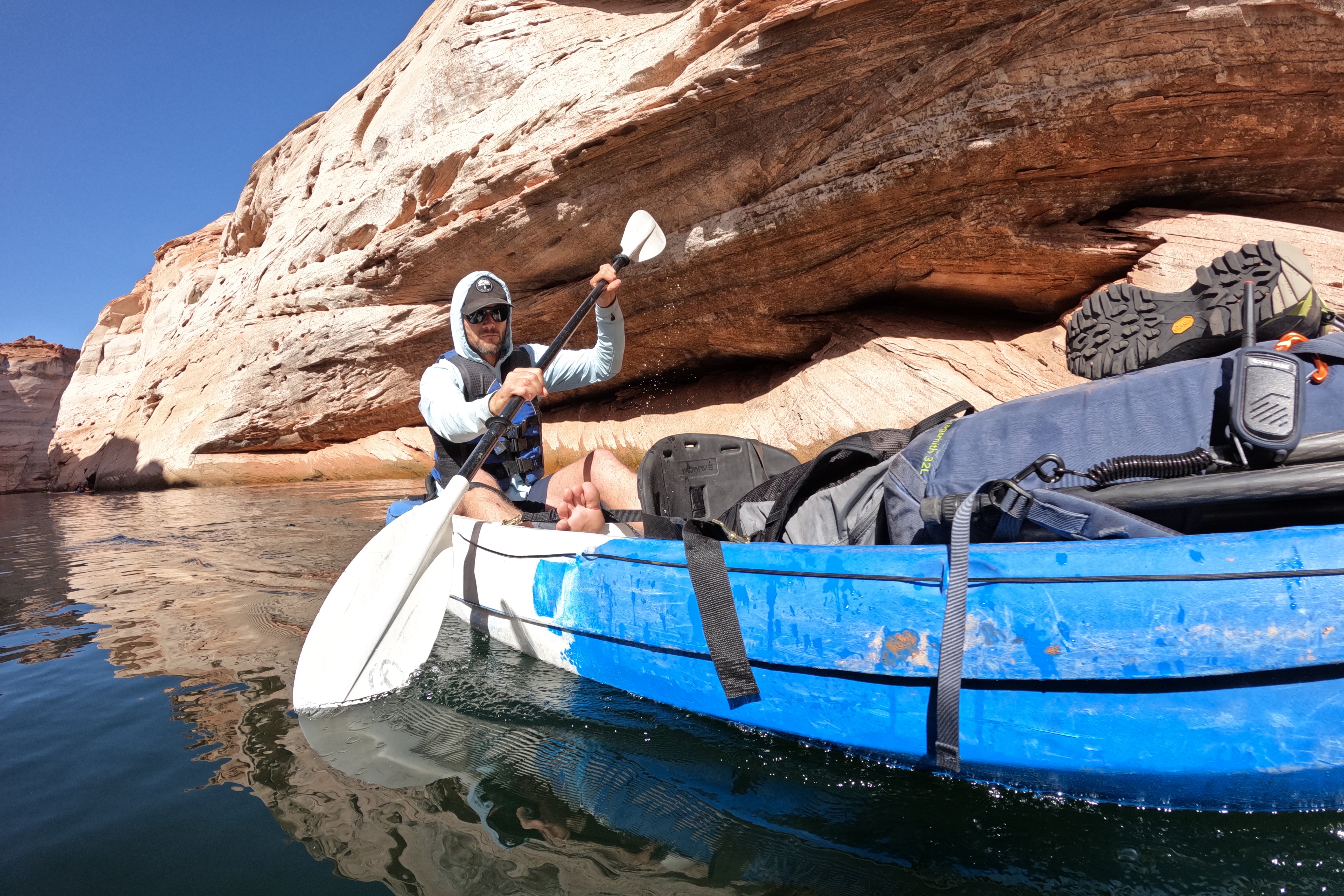 Man kayaking through a narrow sandstone canyon wearing an ANETIK hooded UPF shirt and hat on calm water