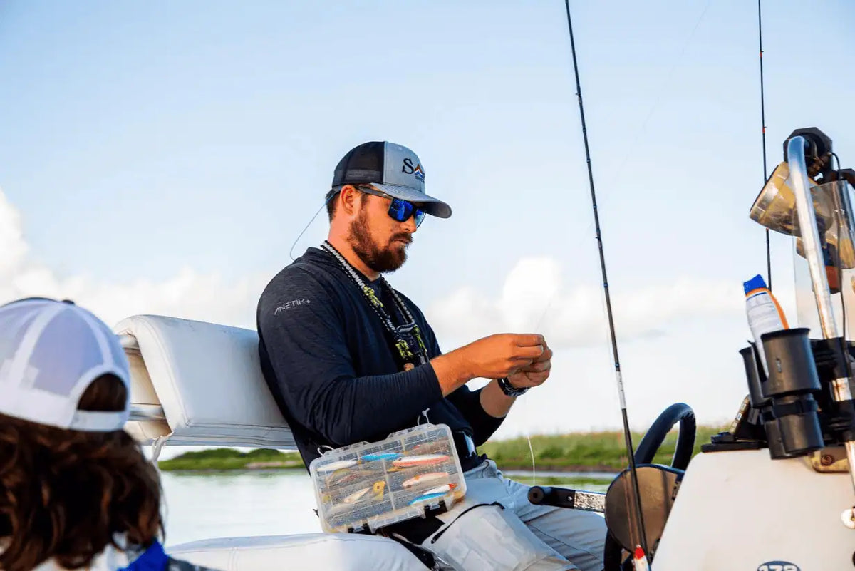 Man preparing fishing tackle aboard a boat, with fishing rods and gear visible around him.