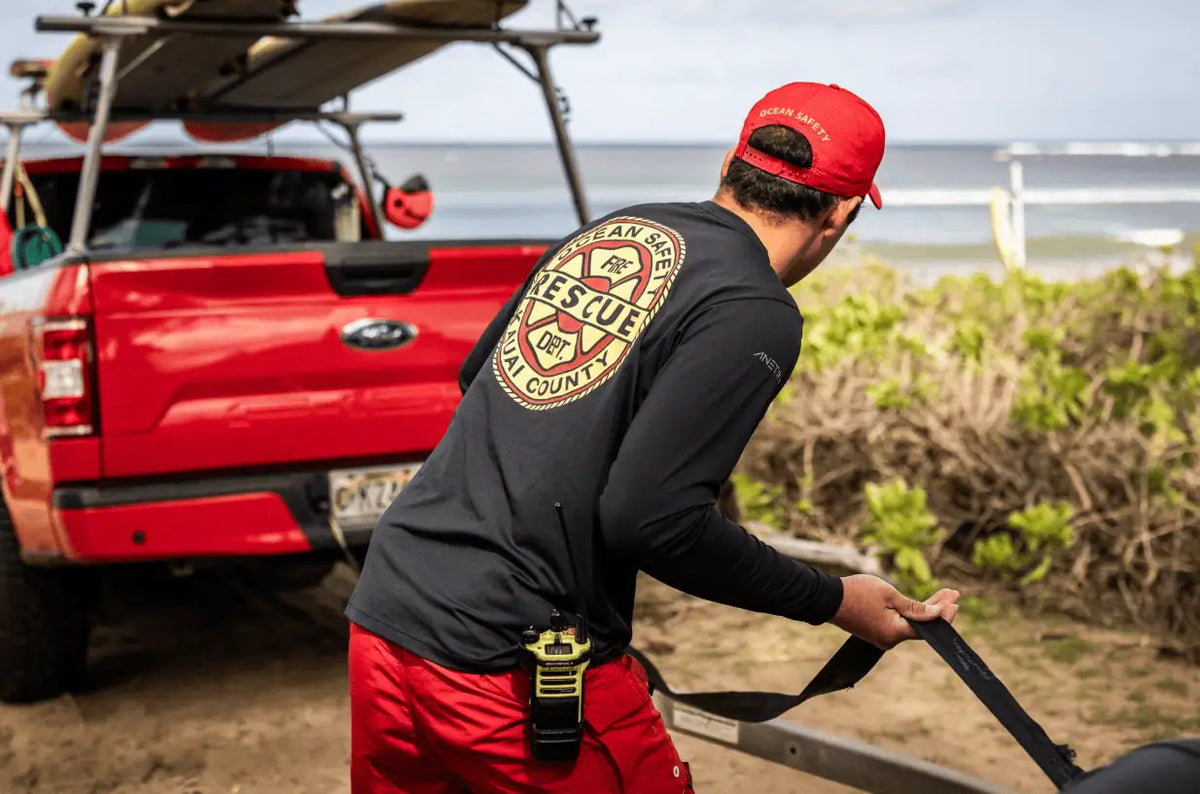 Kauai ocean safety rescue worker securing equipment beside a red lifeguard truck with kayaks near the beach.